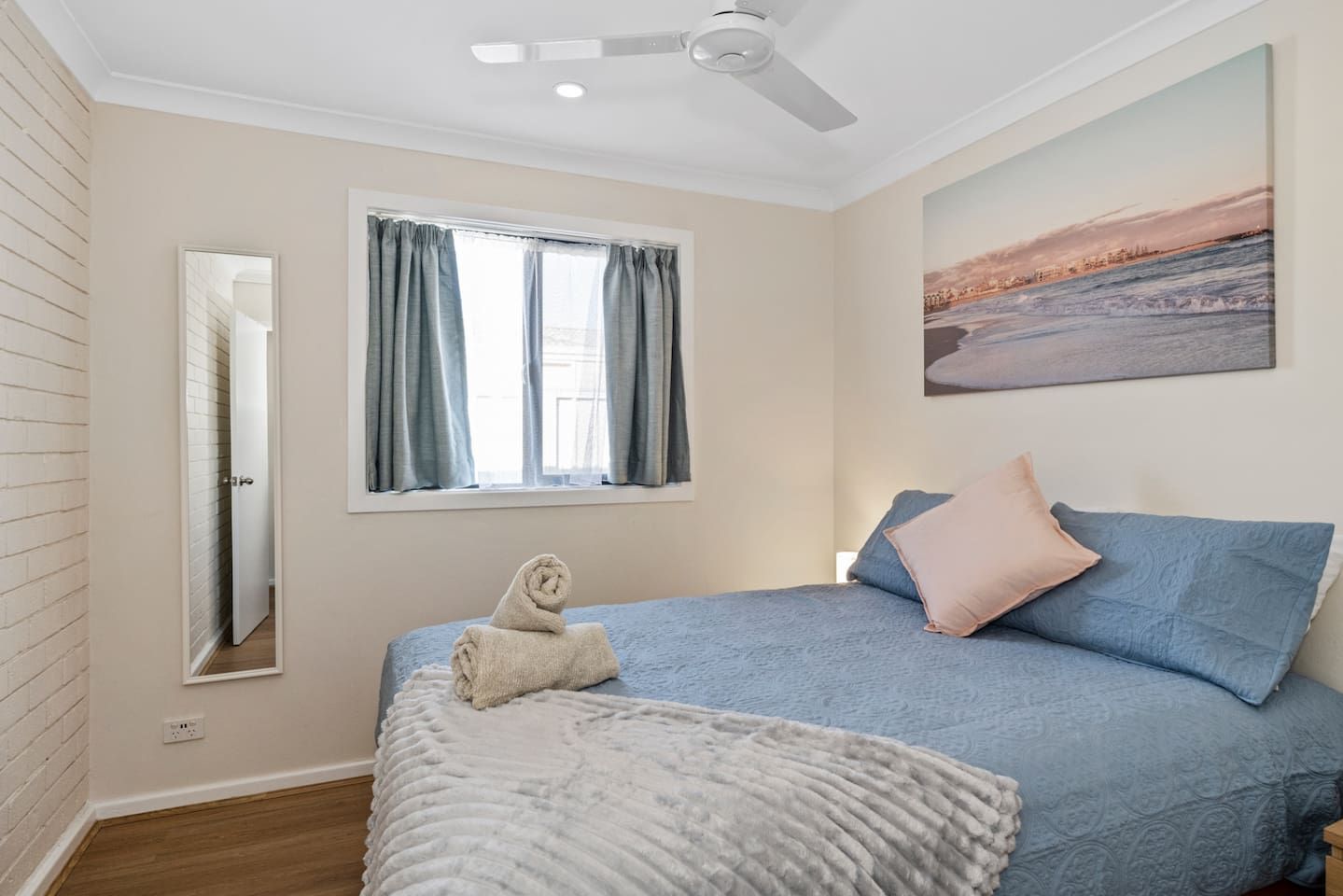 Ein Schlafzimmer mit einem Bett, einem fenster mit Vorhängen, einem Deckenventilator, einem Bild an der Wand und einem Handtuch auf dem Bett.