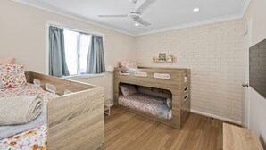 A child's bedroom with a bunk bed, a ceiling fan, a window with curtains, and a brick-patterned wall. - Sandy Shores Getaway (Mandurah)