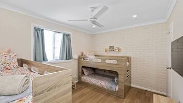 A child's bedroom with a bunk bed, a ceiling fan, a window with curtains, and a brick-patterned wall.
