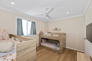 A child's bedroom with a bunk bed, a ceiling fan, a window with curtains, and a brick-patterned wall.