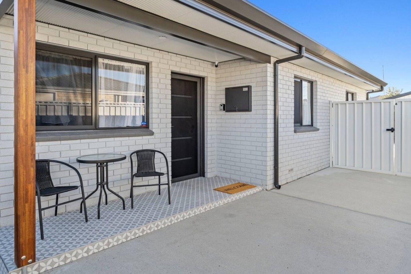 A building with a tiled exterior, a door, and a small patio area with two chairs and a table.