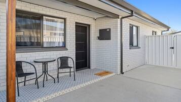 A building with a tiled exterior, a door, and a small patio area with two chairs and a table.