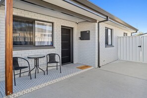A building with a tiled exterior, a door, and a small patio area with two chairs and a table. - Sandy Shores Getaway (Mandurah)