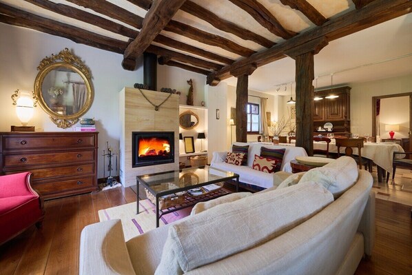 A cozy living room with a fireplace, wooden beams, a sofa, and a dining area.