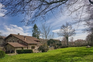 A stone house with a sloped roof, surrounded by a grassy area and trees.