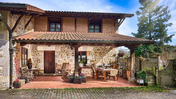 A stone house with a tiled roof, a covered patio with furniture, and a wooden fence. - The Basque Experience by Fidalsa (Otxandio)