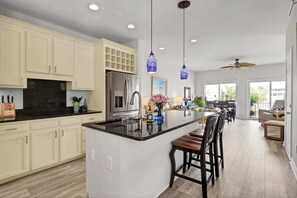 A modern kitchen with a central island, pendant lights, and a dining area with a view.