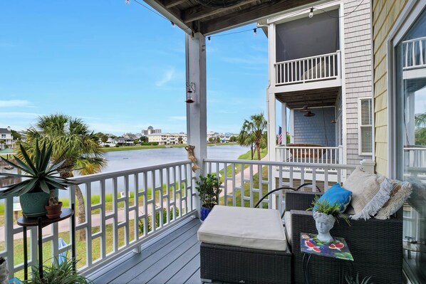 A balcony with a view of a body of water, a potted plant, and a wicker sofa with cushions.