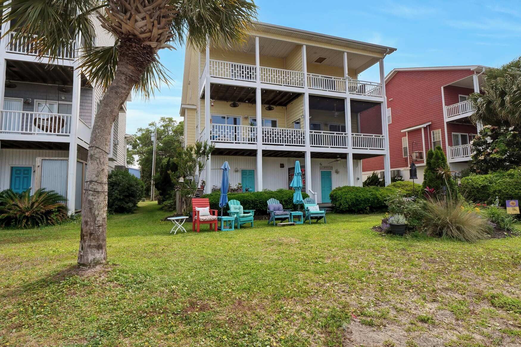 A two-story building with a covered front porch, outdoor seating area with chairs and umbrellas, and a red building adjacent to it.