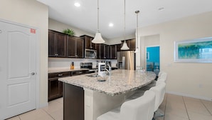 A modern kitchen with dark cabinets, granite countertops, stainless steel appliances, and a central island with bar seating. - Family home w/ private pool near Disney (Kissimmee)