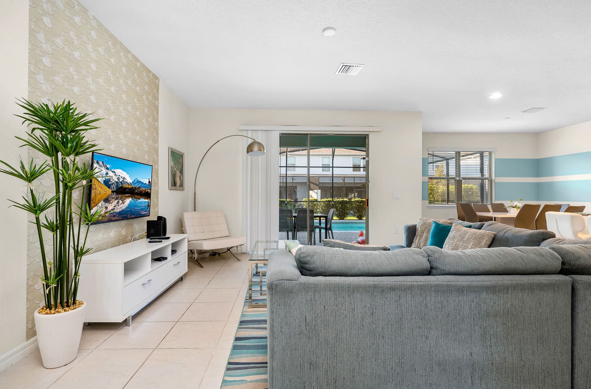 A modern living room with a grey sofa, a white entertainment unit, a large flat-screen TV, and a potted plant.