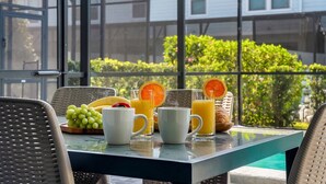 A breakfast table with fruits, juice, and pastries, overlooking a pool and greenery. - Family home w/ private pool near Disney (Kissimmee)