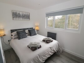 A modern bedroom with a large bed, bedside lamps, a radiator, and a window with a view of trees.