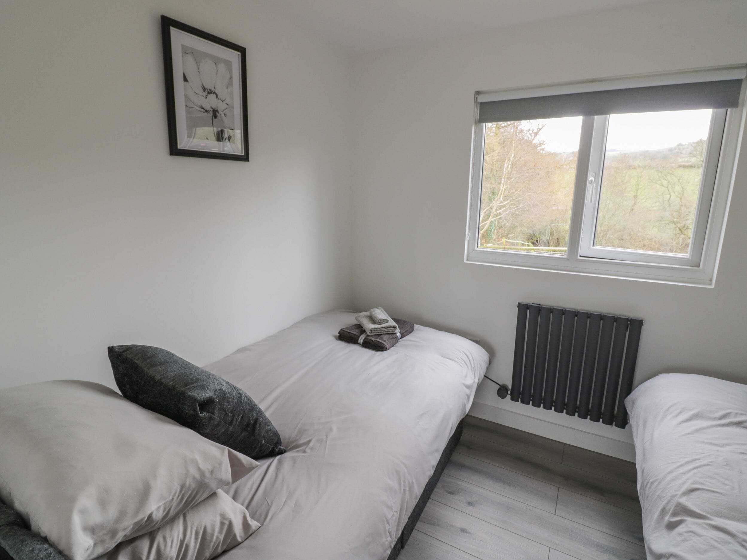 A bedroom with a bed, pillows, a radiator, a window, and a framed picture on the wall.