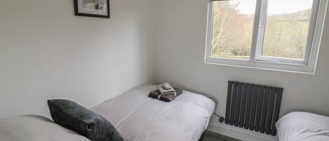 A bedroom with a bed, pillows, a radiator, a window, and a framed picture on the wall.