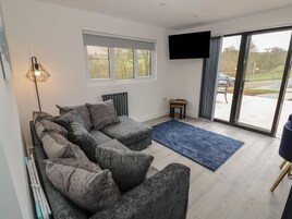 A modern living room with a sectional sofa, a flat-screen TV, a small table, and a large sliding glass door leading to an outdoor area.