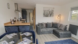 Ein modernes Wohnzimmer mit einem grauen Ecksofa, einem Glastisch und einem blauen Teppich.