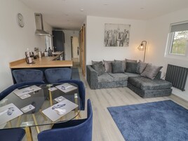 A modern living room with a grey sectional sofa, a glass coffee table, and a blue rug.