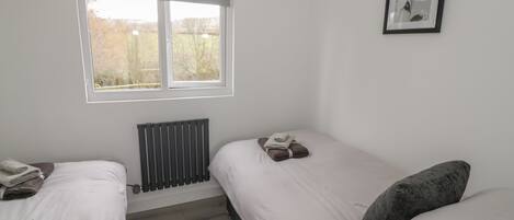 A bedroom with two single beds, a radiator, a window with a view of trees, and a framed picture on the wall.