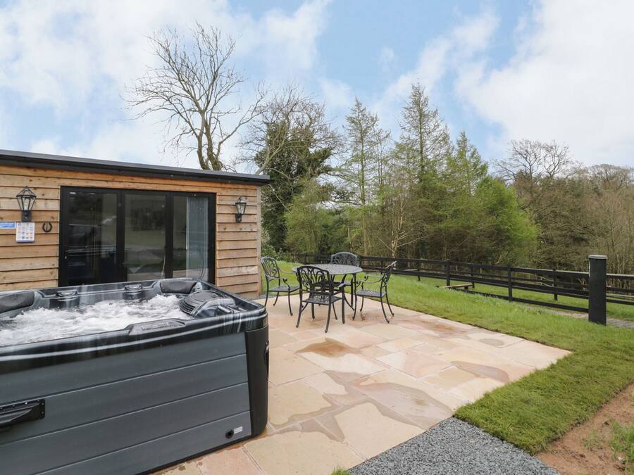A hot tub outside a wooden building with a patio table and chairs.