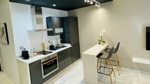 A modern kitchen with dark cabinetry, a white countertop, and a built-in oven. There is a small bar area with two chairs and a vase of flowers. - StayInn Maarif Downtown (Casablanca)
