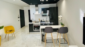A modern kitchen with a white countertop, black cabinets, and a black ceiling. There are two chairs with wooden legs and a small table. - StayInn Maarif Downtown (Casablanca)