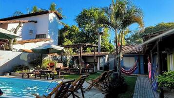 A pool area with lounge chairs, a paved walkway, and a building with a tiled roof.