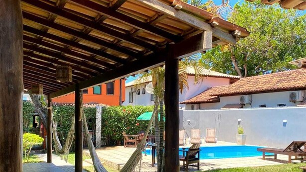 A covered outdoor area with a hammock, a pool, and a patio with chairs and tables. - Pousada Tropicália (Porto Seguro)
