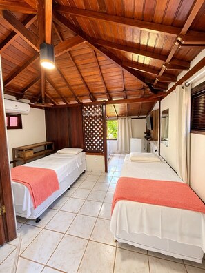 A room with two beds, a wooden ceiling, a window, and a small table. - Pousada Tropicália (Porto Seguro)