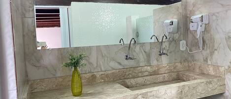 A bathroom with a marble sink, a mirror, a hairdryer, and a vase with a plant.
