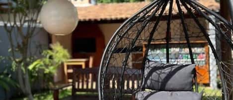 Une chaise suspendue avec des coussins, placée sur une terrasse en bois, avec une table et un lampadaire, le tout dans un cadre de jardin.