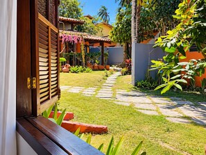 A garden pathway leading to a wooden door with a window, surrounded by lush greenery and potted plants. - Pousada Tropicália (Porto Seguro)