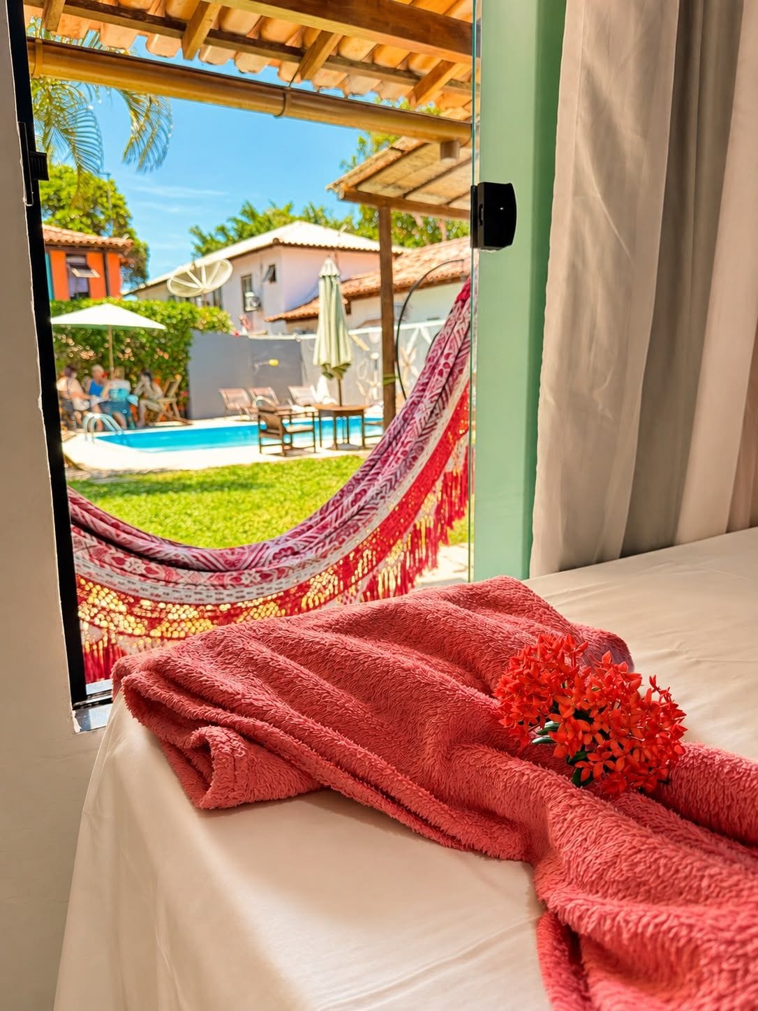 A room with a bed, a hammock, and a view of a swimming pool.
