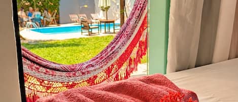 A room with a bed, a hammock, and a view of a swimming pool.