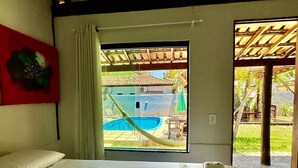 A hotel room with a bed, a view of a swimming pool, and a patio area. - Pousada Tropicália (Porto Seguro)