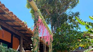 A garden with a pergola covered in pink flowers, a brick building, and terracotta pots. - Pousada Tropicália (Porto Seguro)