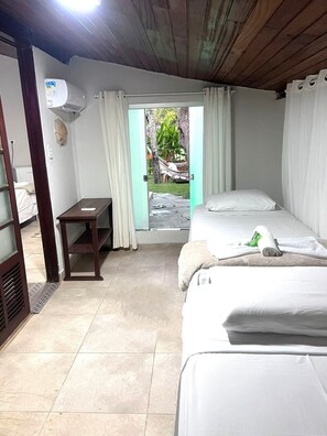 A small, well-lit room with two beds, a wooden desk, and a window with curtains. - Pousada Tropicália (Porto Seguro)