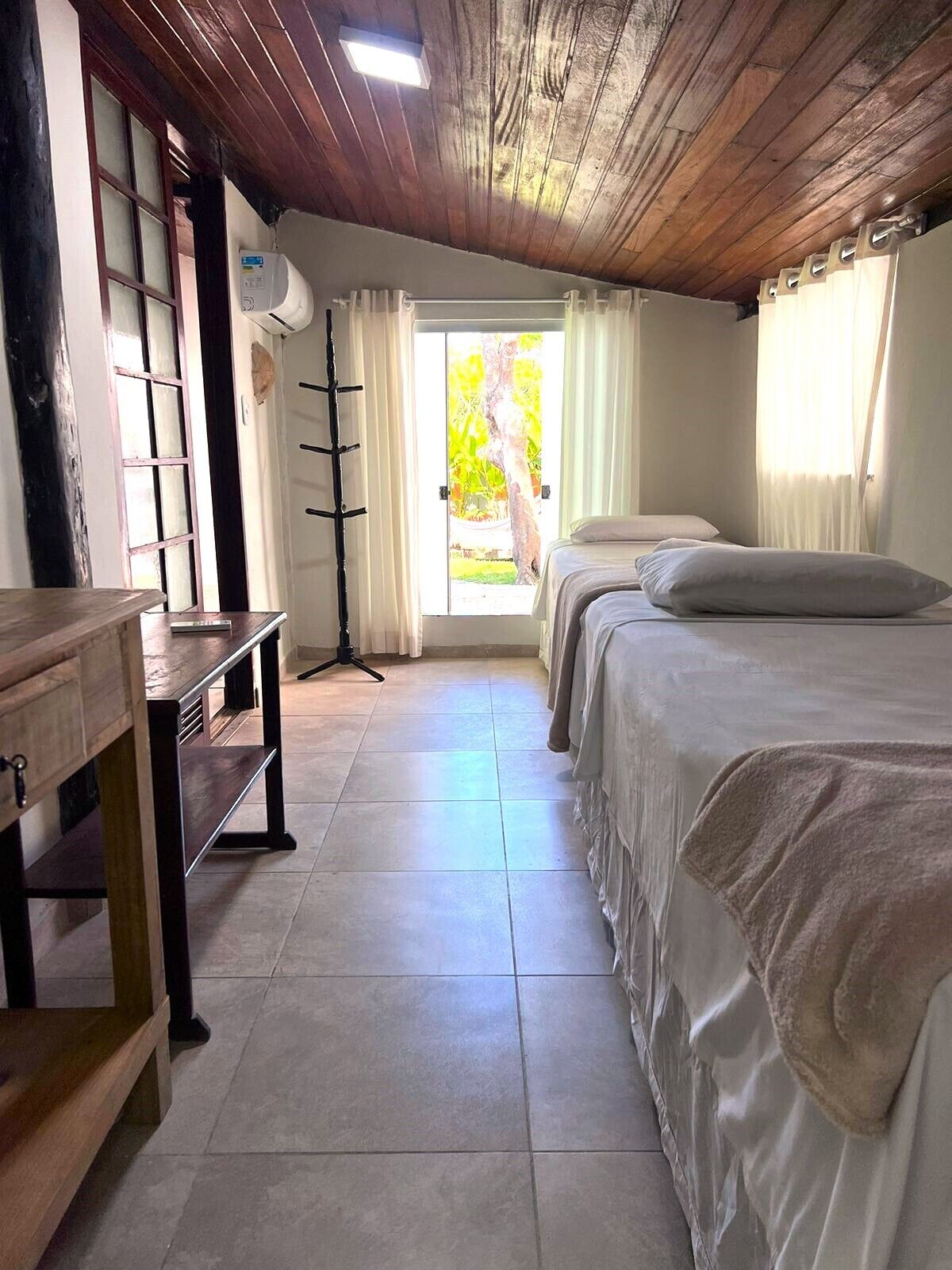 A room with two beds, a wooden desk, and a large window with curtains.