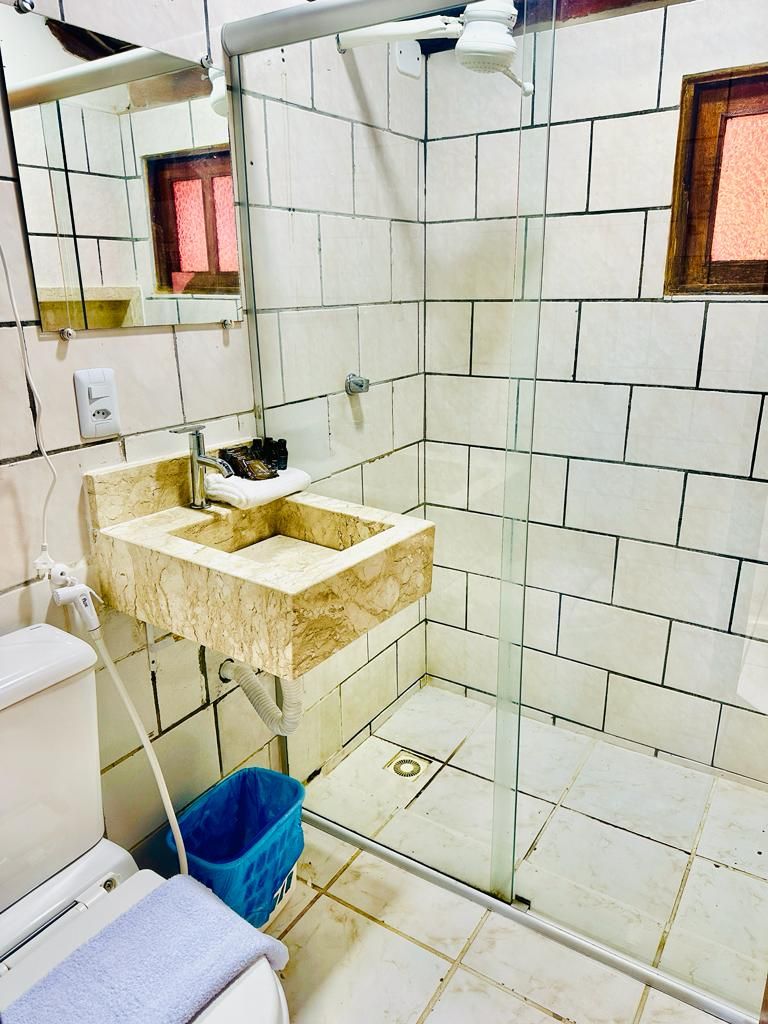 A bathroom with a glass-enclosed shower, a marble sink, and a blue trash bin.