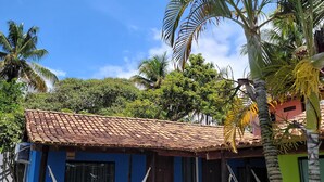 A blue house with a tiled roof, a hammock, and a palm tree. - Pousada Tropicália (Porto Seguro)