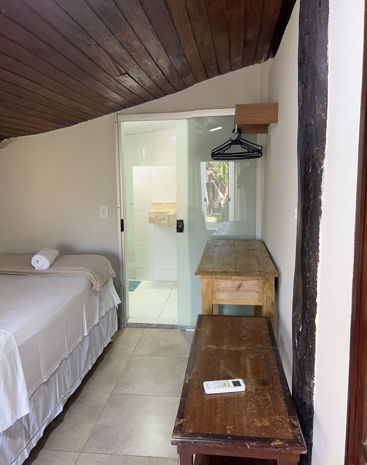 A bedroom with a bed, a wooden bench, a hanging light, and a door leading to a balcony.