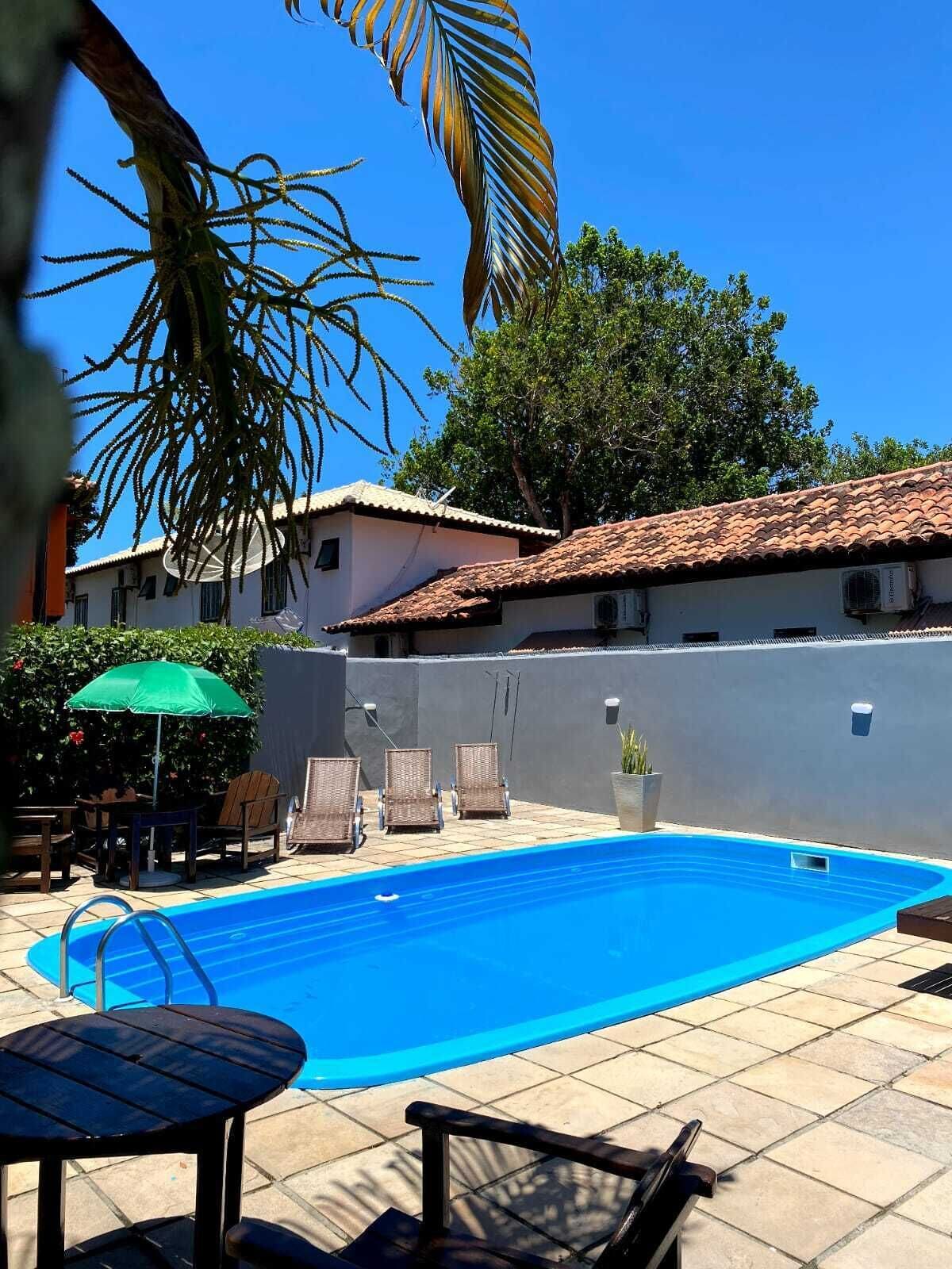 A swimming pool with lounge chairs and a table, surrounded by a building with a tiled roof and a grey wall.