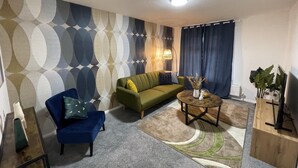 A living room with a green sofa, blue armchair, and a round coffee table with a vase and plant. - Convenient 3 bd House Salford 7 Guests (Salford)