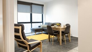 A modern living room with a sectional sofa, a dining table with chairs, a yellow rug, and large windows with blinds. - St Kilda Rd Gem | Prime Spot (Melbourne)