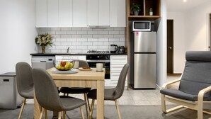 A modern kitchen with white cabinets, a stainless steel refrigerator, a microwave, and a dining area with a table and chairs. - St Kilda Rd Gem | Prime Spot (Melbourne)