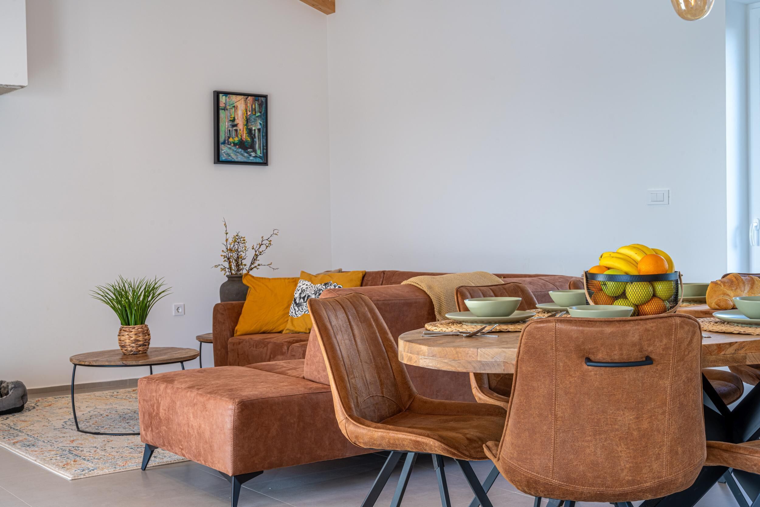 Un espace repas moderne avec une table ronde en bois, des chaises à revêtement marron et un panier de fruits posé sur la table.