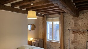 Una camera da letto con un letto, una lampada a sospensione, uno specchio, una finestra con tende e un muro in mattoni.