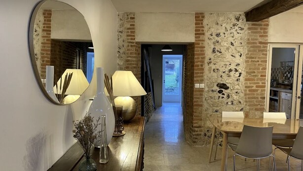 Una cucina moderna con parete in mattoni, un'area pranzo con tavolo e sedie, e un corridoio che porta a una porta.