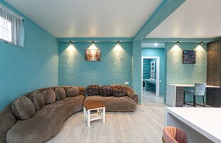A modern living room with a curved sofa, a small wooden table, and a kitchen area with a white countertop and chairs.