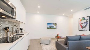 Eine moderne Küche mit Einbauherd, ein Essbereich mit grauem Sofa und kleinem Tisch sowie ein Wohnzimmer mit grauem Sofa und einem Gemälde an der Wand.